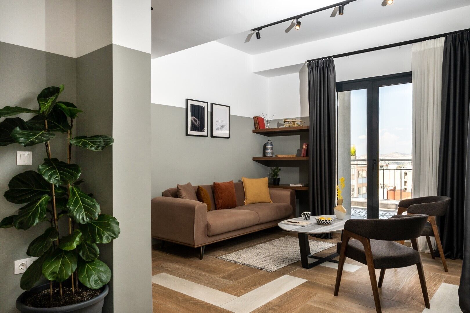 A modern living room with a sofa, coffee table, and chairs. There is a large window with curtains, a plant, and framed pictures on the wall.