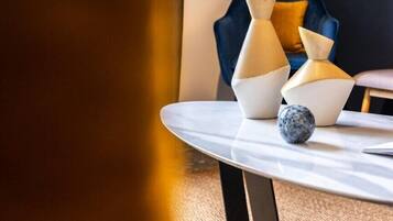 A modern interior with a round table featuring geometric vases and a spherical object, set against a dark blue chair and a textured wall.