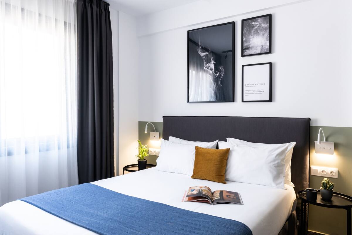 A neatly made bed with a blue throw blanket, white pillows, and a single brown pillow. There are three framed pictures on the wall above the bed.