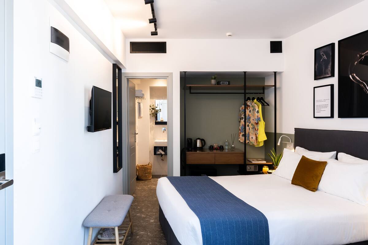 A modern hotel room with a large bed, a seating area, a wardrobe, and a small desk.