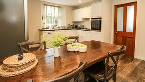 A modern kitchen with white cabinets, a wooden dining table, and a refrigerator. - Old Schoolhouse (Aberfeldy)