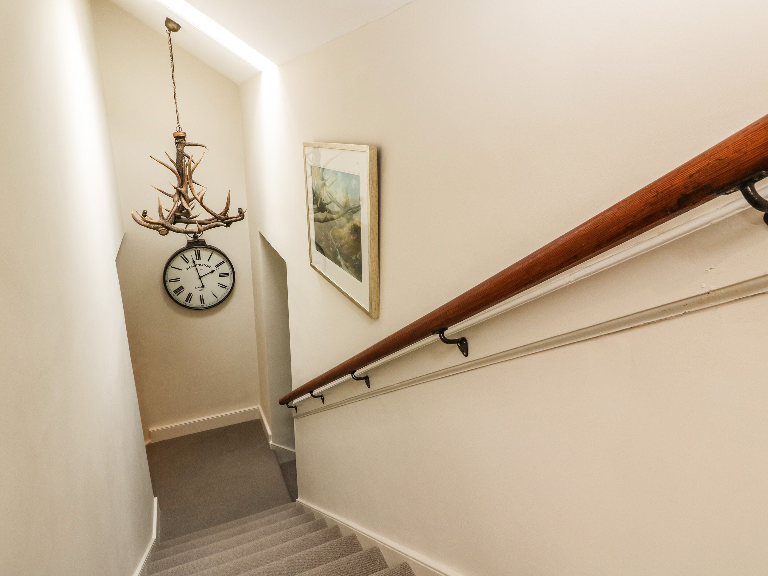 Una escalera con barandilla de madera, un reloj de pared y un cuadro enmarcado.