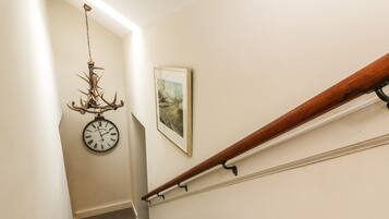 Una escalera con barandilla de madera, un reloj de pared y un cuadro enmarcado.