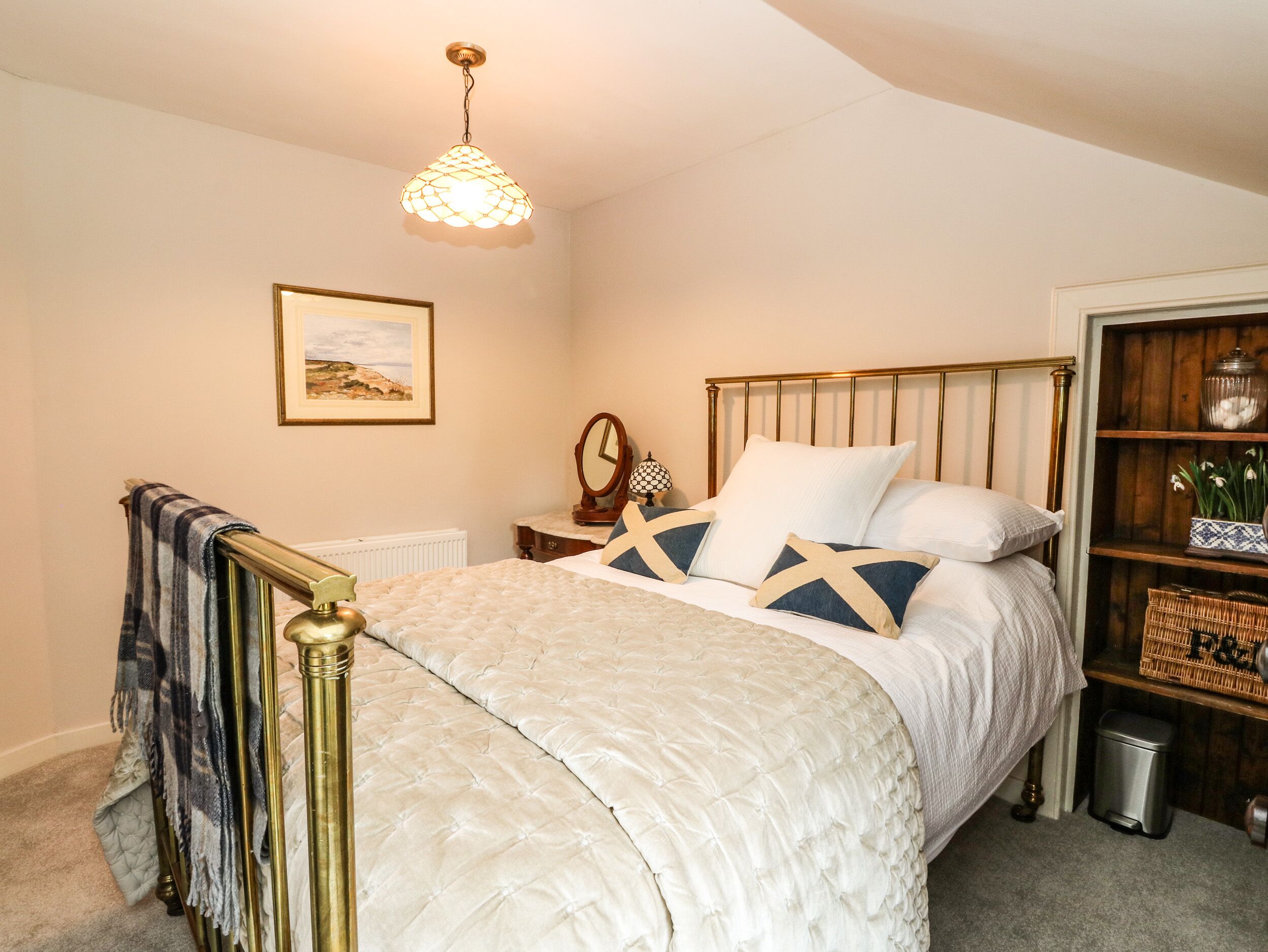 A bedroom with a bed, a nightstand, a mirror, a picture on the wall, and a shelf with decorative items.