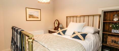 A bedroom with a bed, a nightstand, a mirror, a picture on the wall, and a shelf with decorative items.