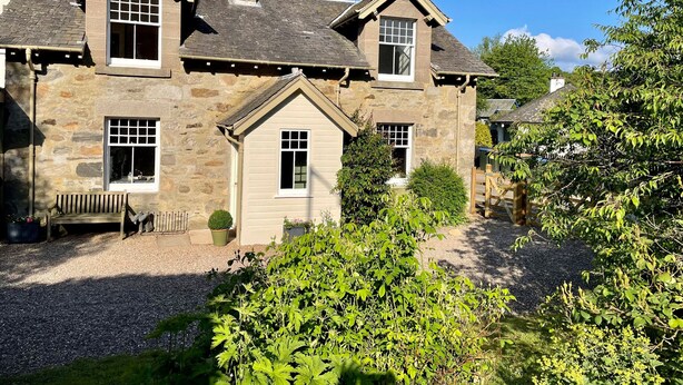 A stone house with a chimney, multiple windows, and a gravel driveway. - Old Schoolhouse (Aberfeldy)