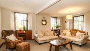 A living room with a sofa set, a wooden coffee table, and a chair with a fur throw. - Old Schoolhouse (Aberfeldy)