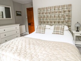 Un dormitorio con cama, cómoda, mesita de noche, lámpara y puerta.
