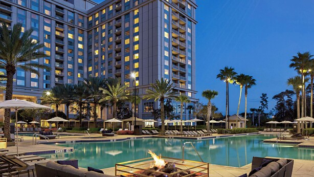 A hotel with a swimming pool, lounge chairs, and palm trees.