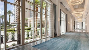 A hotel corridor with large windows, chandeliers, and a blue carpet.