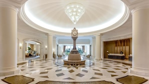 A grand lobby with a central clock, a chandelier, and a patterned floor.