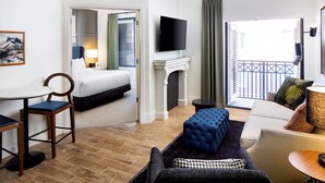 A hotel room with a bed, a TV, a fireplace, a balcony, and a seating area with a sofa and ottoman.