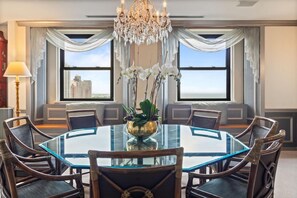 A dining area with a round glass table, wicker chairs, a chandelier, and a view of buildings through large windows. - 2 Connecting Suites at a 4⭐️ Hotel (Chicago)
