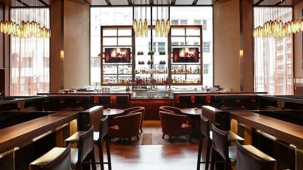 Angolo bar con tavoli e sedie in legno, un bancone e un'ampia finestra con vista sugli edifici.