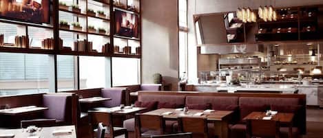 Un restaurante con mesas y bancos de madera, una zona de cocina y un amplio ventanal con vistas.