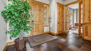 Un pasillo con puertas de madera, una planta en maceta, un tapete y un perchero.