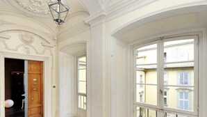 Un pasillo espacioso con piso de diseño geométrico, una puerta de madera y grandes ventanales que ofrecen vistas de edificios vecinos.