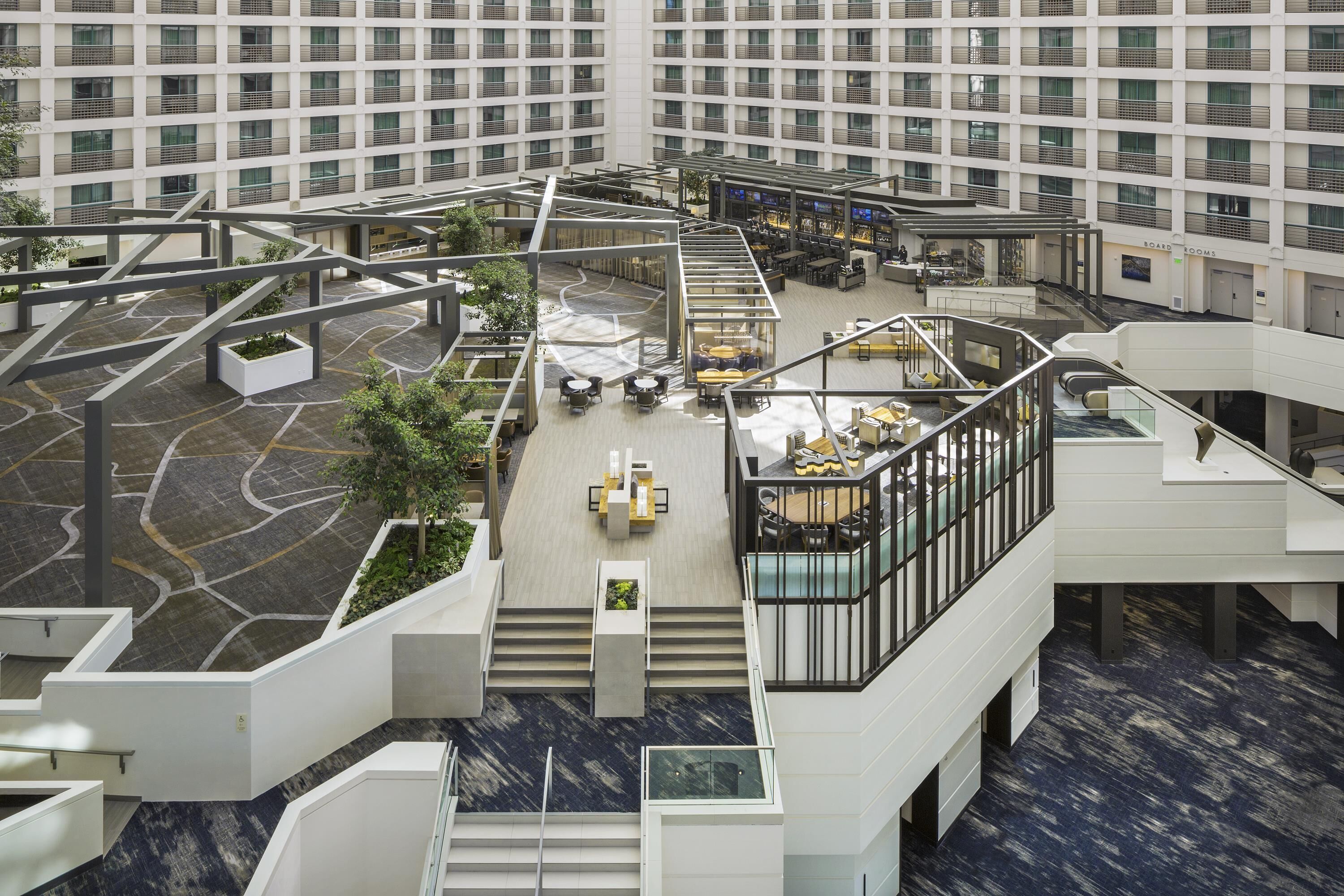 A modern hotel atrium with multiple levels, outdoor seating areas, and a central staircase.