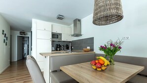 A modern kitchen with white cabinets, a microwave, and a built-in stove. There is a wooden dining table with a fruit bowl and a vase of flowers. - Vacation apartment Ritzhagen in Willingen (Willingen)