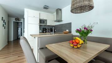 Eine moderne Küche mit weißen Schränken, einer Mikrowelle und einem eingebauten Herd. Es gibt einen Holztisch mit Obstschale und Blumenvase.