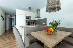 Eine moderne Küche mit weißen Schränken, einer Mikrowelle und einem eingebauten Herd. Es gibt einen Holztisch mit Obstschale und Blumenvase.