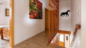 Una escalera de madera con la silueta de un caballo negro en la pared, un piso de madera y un cuadro de flores en la pared.