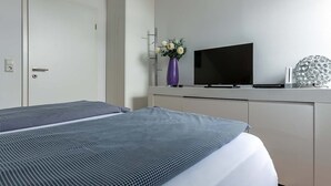 Een moderne hotelkamer met een bed, een televisie, een vaas met bloemen en een decoratief object op het nachtkastje.