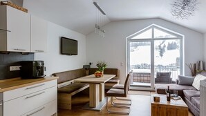 Een moderne keuken met een koffieapparaat, een eettafel met stoelen en een groot raam met uitzicht op een besneeerd landschap.