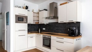Een moderne keuken met witte kasten, een magnetron, een fornuis en een koffiezetapparaat.