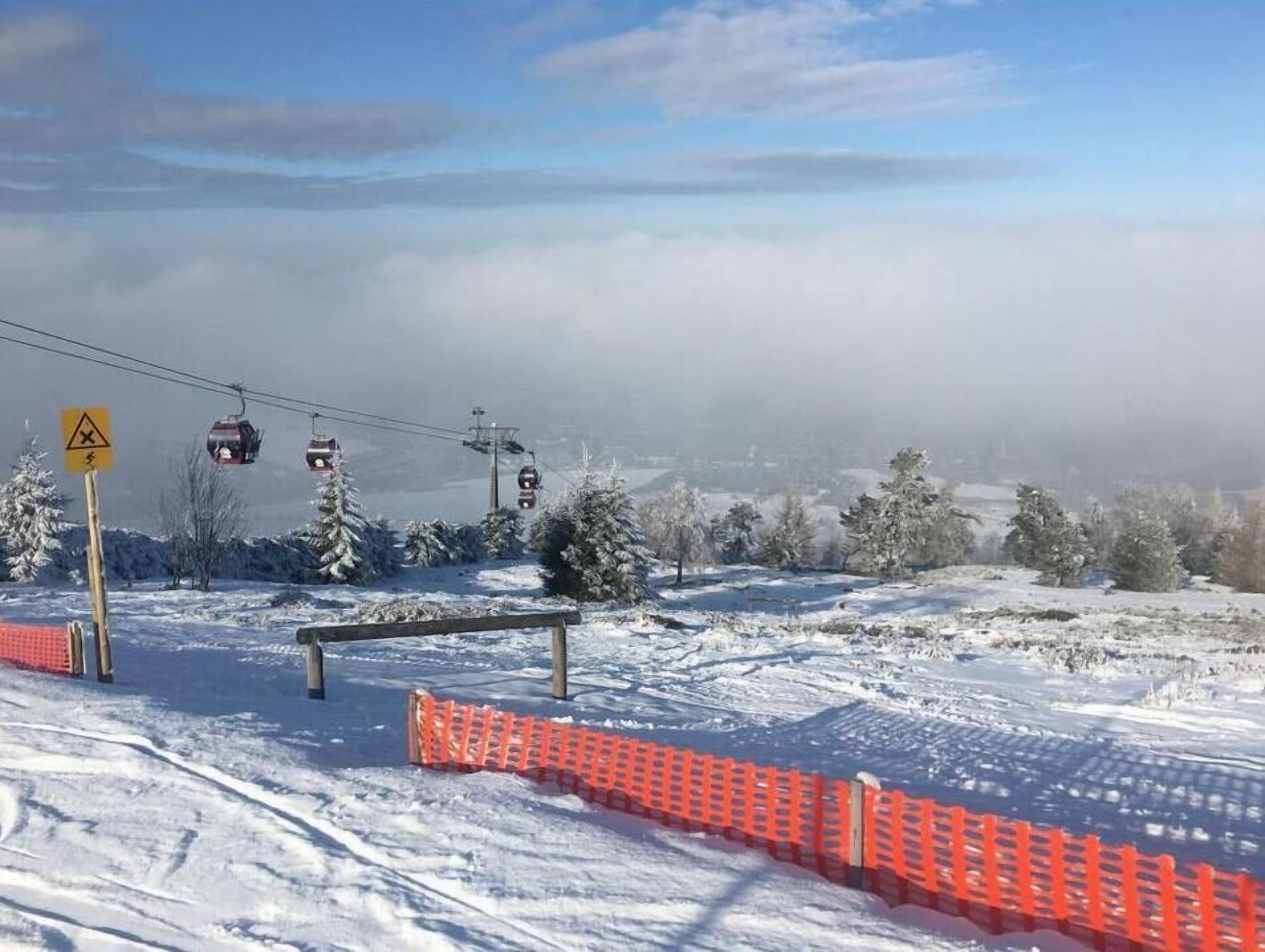 Een besneeerd landschap met een skilift, een rode veiligheidshek en een waarschuwingsbord.