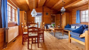 Puinen mökki, jonka sisustuksessa on ruokapöytä, tuoleja, sohva ja kattokruunu.