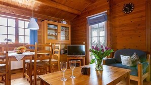 Tunnelmallinen mökin sisustus, jossa on ruokailutila, olohuone sohvineen ja televisiineen sekä lasiovilla varustettu kaappi.