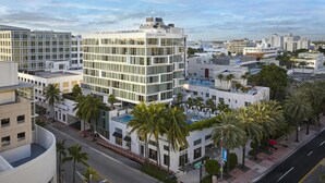 Un hôtel à plusieurs étages doté d’une façade moderne en verre, situé dans un quartier urbain bordé de palmiers et entouré d’autres bâtiments.