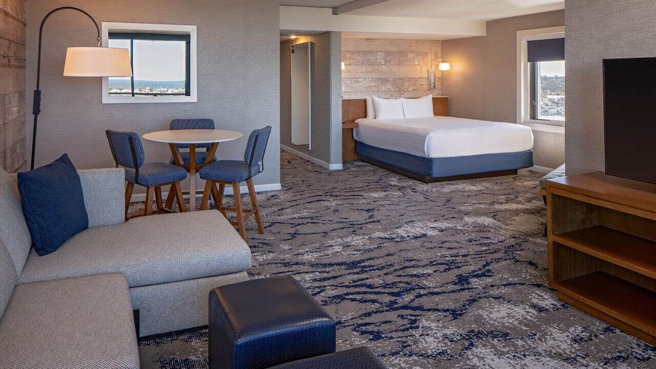 A hotel room with a bed, a sofa, a small table with chairs, a lamp, and a TV.