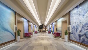 Eine Hotelhalle mit einer zentralen Rezeption, Sitzbereichen und großer abstrakter Wandkunst.