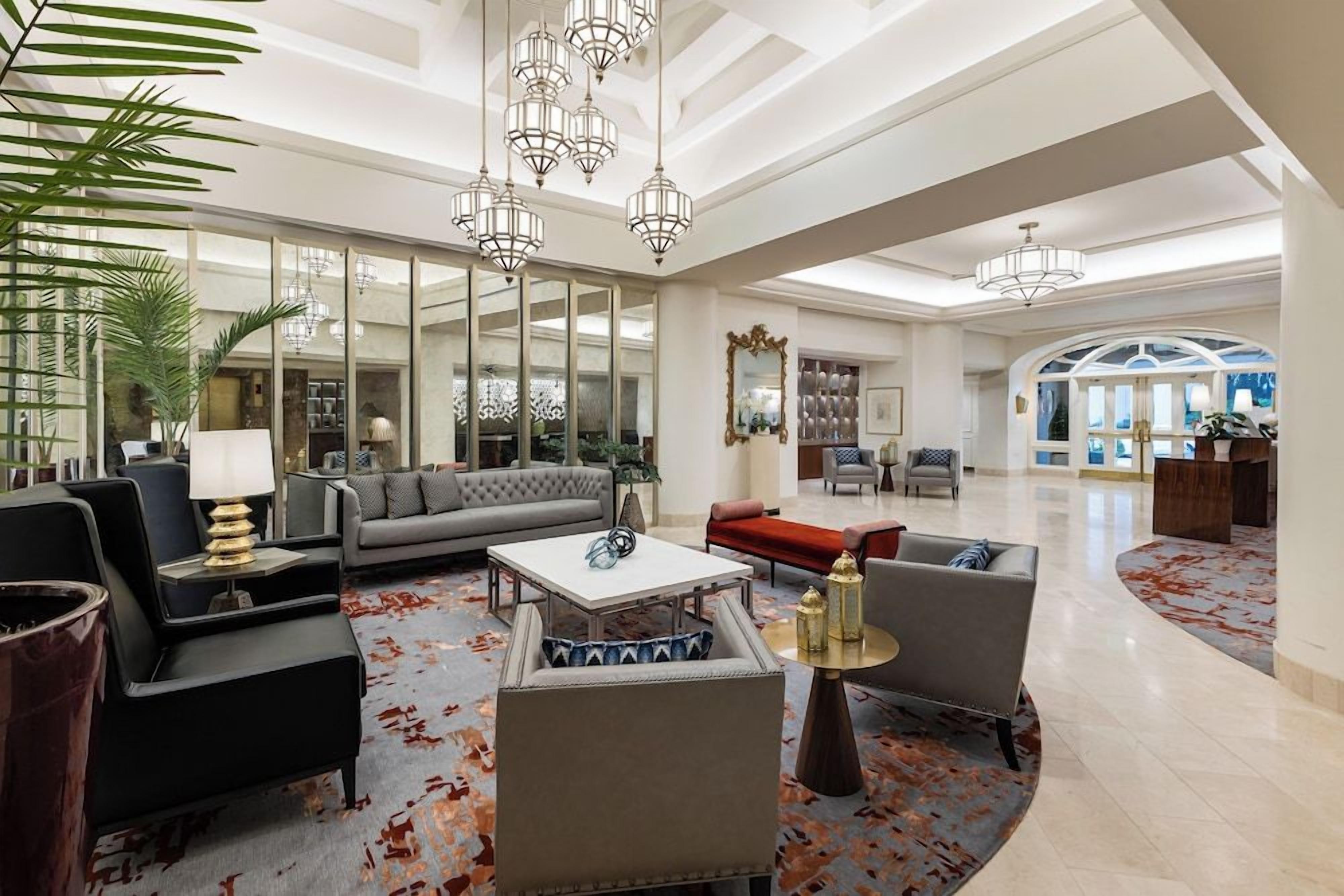 Eine großzügige Lobby mit hoher Decke, modernen Kronleuchtern und einer Mischung aus Sitzgelegenheiten, darunter Sofas und Sessel.