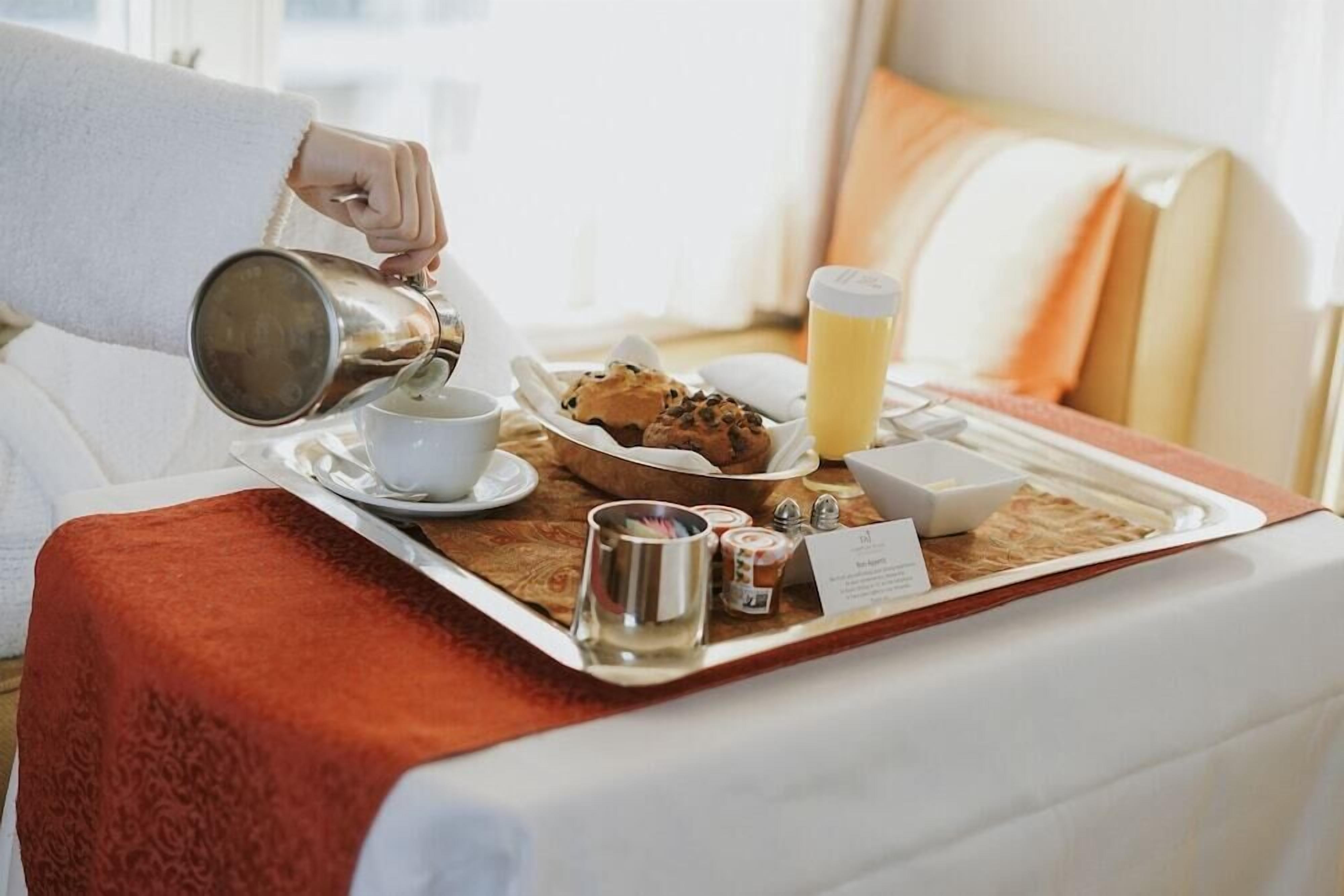 A breakfast tray with a cup, muffin, juice, and condiments on a bed.
