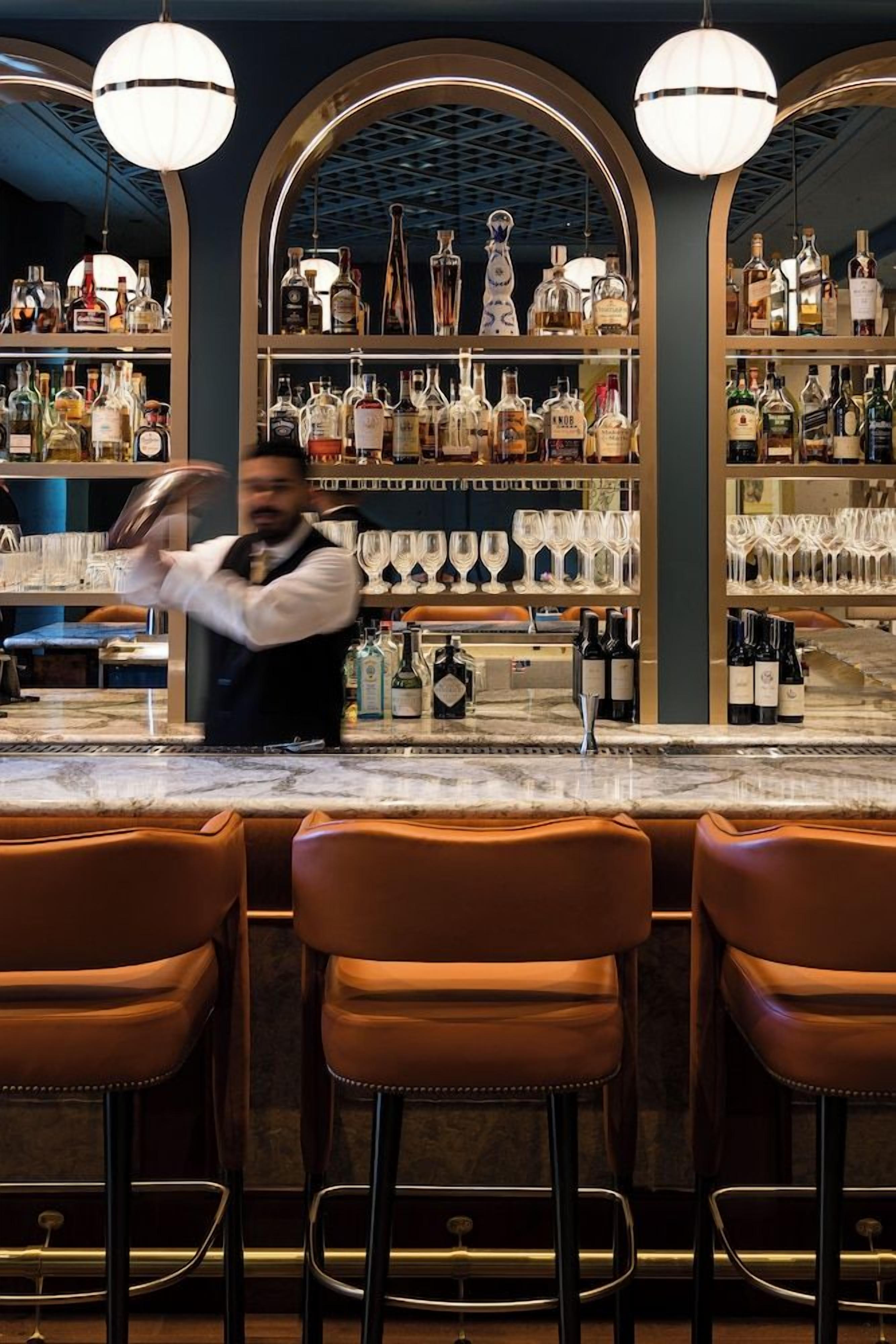 Eine Bar mit einem Barkeeper, der Getränke zubereitet, Regalen voller Spirituosenflaschen und Barhocker.