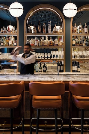 A bar area with a bartender preparing drinks, shelves of liquor bottles, and bar stools. - 2 Connecting Suites at a 5⭐️ Hotel (San Francisco)