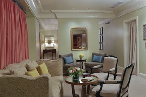A living room with a sofa, armchairs, a coffee table with books and flowers, a mirror, and a door leading to another room. - 2 Connecting Suites at a 5⭐️ Hotel (San Francisco)