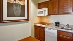 A kitchen with wooden cabinets, a microwave, a dishwasher, and a framed painting on the wall. - 2 Connecting Suites at a  Hotel (Houston)