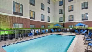 A swimming pool with lounge chairs and umbrellas, surrounded by a brick wall and windows. - 2 Connecting Suites at a  Hotel (Houston)