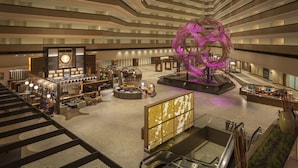 En moderne hotellobby med et centralt siddeområde, en stor dekorativ skulptur og en bar.