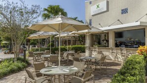 An outdoor seating area with tables and chairs, umbrellas, and a bar area with a sign for Coconuts Poolside Bar & Grill. - 2 Connecting Suites at a 4.5⭐️ Hotel (Orlando)