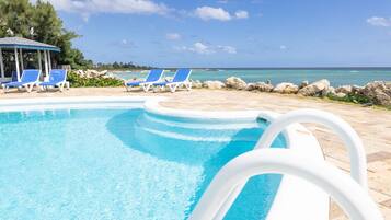 A pool area with clear blue water, blue lounge chairs, and a view of the ocean.