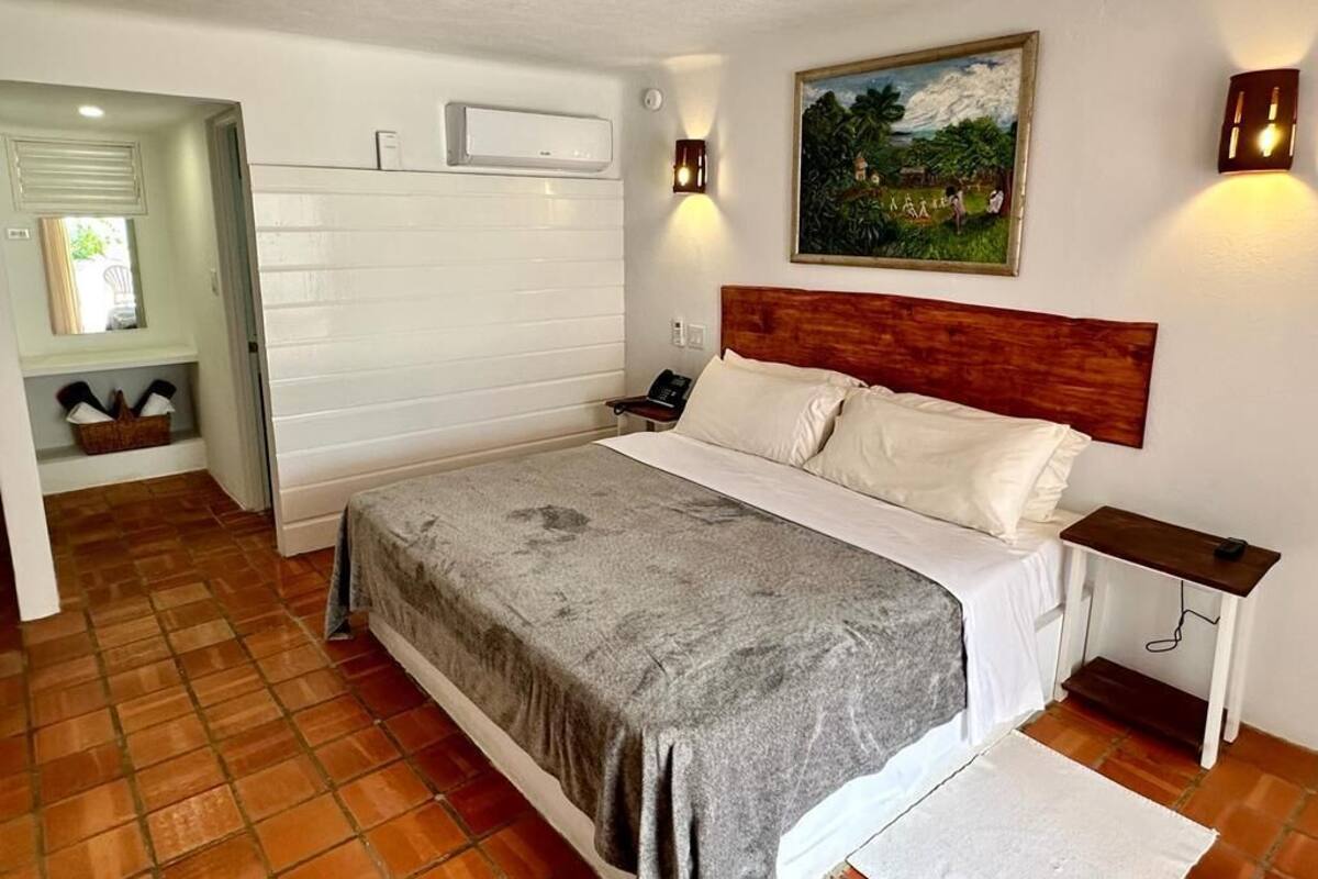 Ein Schlafzimmer mit Bett, Nachttisch, Wandklimaanlage, einem Gemälde und einer Tür zu einem anderen Raum.
