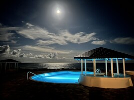 Zona de piscina nocturna con vista despejada al océano y un cielo iluminado por la luna.