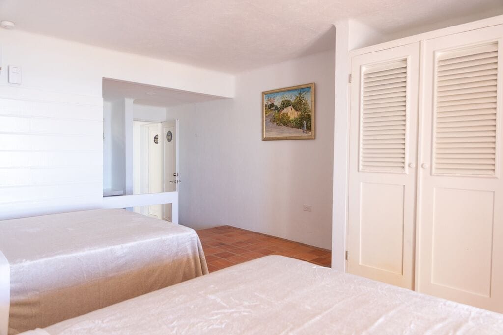 Une chambre avec deux lits, une porte donnant sur une autre pièce, un tableau au mur et une armoire.