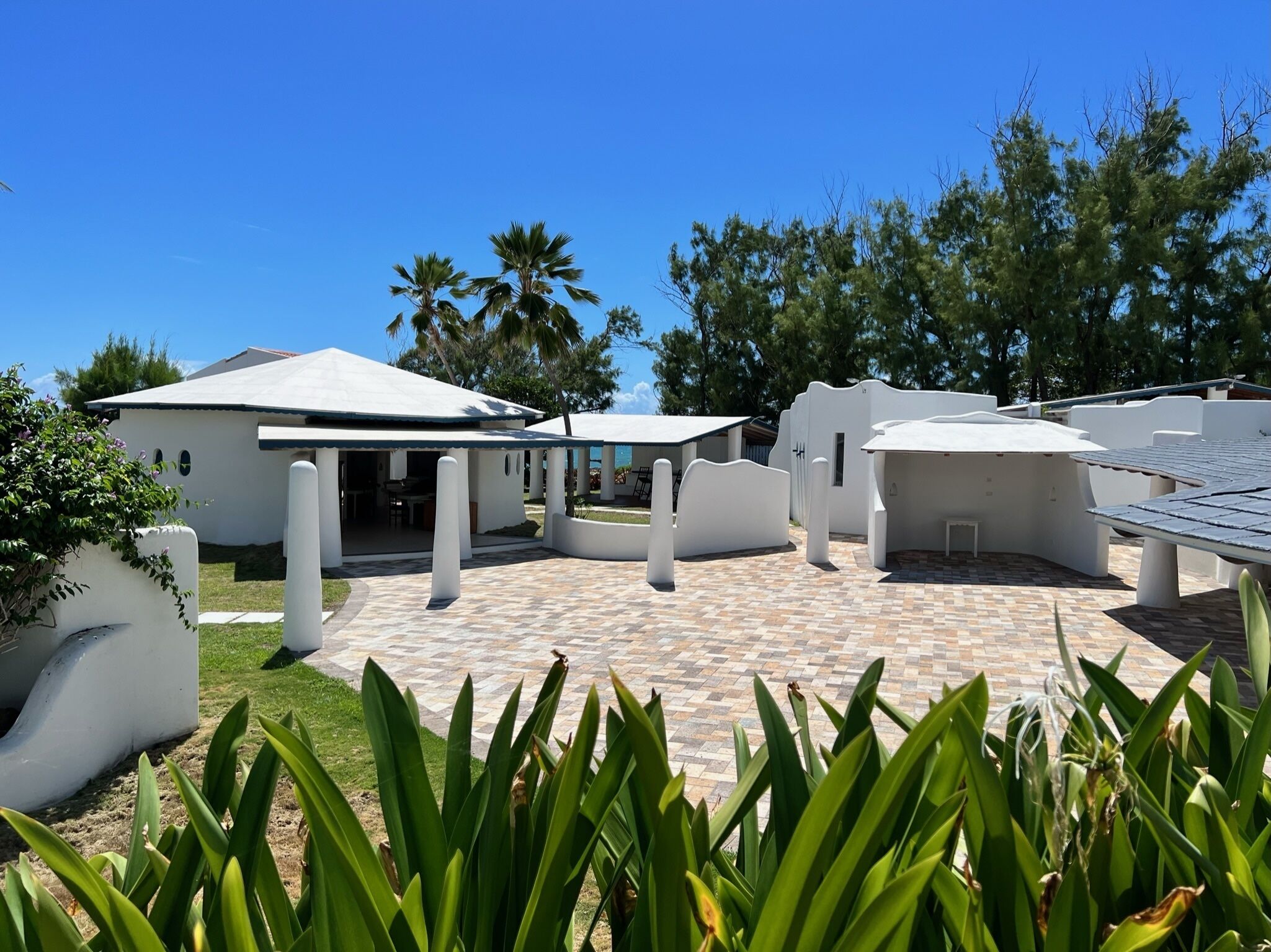 A modern resort with white buildings, a covered patio area, and lush greenery.
