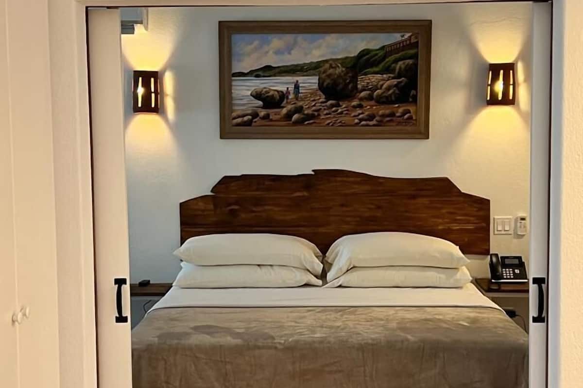 Ein Schlafzimmer mit einem Bett, zwei Nachttischlampen, einem Bild an der Wand und einem Telefon auf dem Nachttisch.